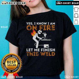 Metal worker in a welding mask, focused on finishing a weld, wearing 'Yes I Know I'm On Fire' ladies tee.