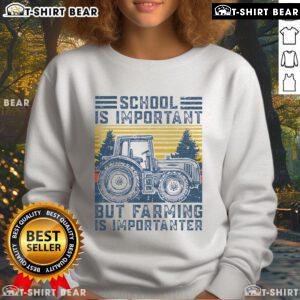 Farmer wearing a sweatshirt with 'Top School Is Important But Farming Is Importanter' slogan, standing next to a tractor on the farm.