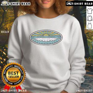 Model wearing a Nice Sunny Shore Wituka sweatshirt on the beach, showcasing a vibrant seaside style.