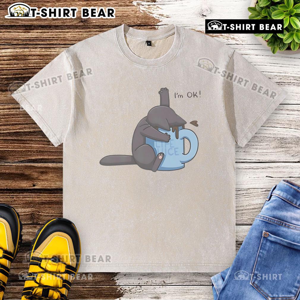 Cute cat playfully submerged in a coffee cup, wearing a I'm okay washed t-shirt, showcasing a humorous moment.