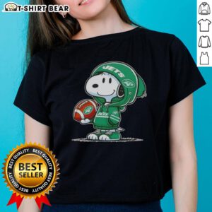 Official Peanuts Snoopy in a hoodie smiling at fans, promoting New York Jets ladies tee merchandise.