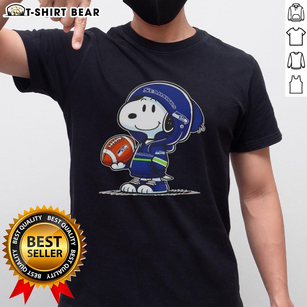 Snoopy in a Seattle Seahawks hoodie smiles at fans on a t-shirt, showcasing Peanuts character in sports gear.