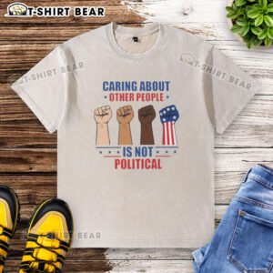 Nice caring about other people is not political fists washed t-shirt displayed on a hanger in a bright room.